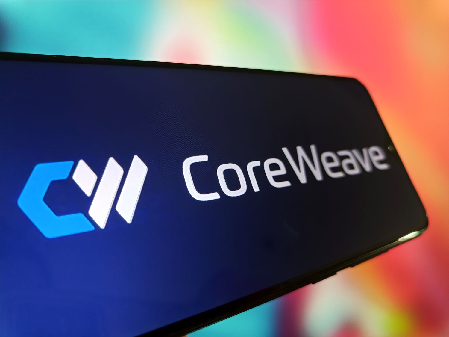 The CoreWeave logo is seen on a phone screen against a colorful background.