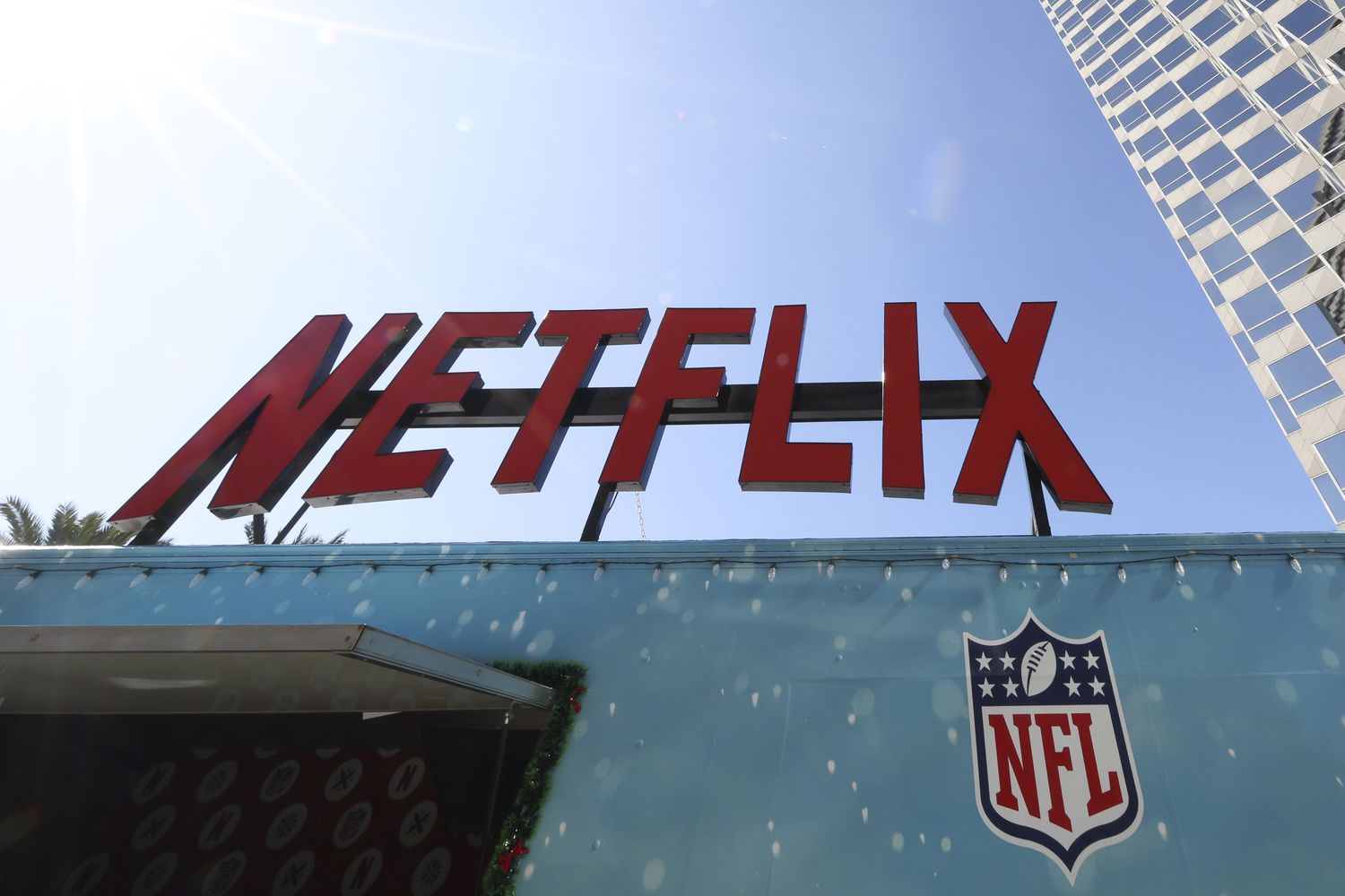 Netflix - Wants the Super Bowl, but not a NFL Package 3 July 4, 2025 9:20 pm Netflix - Wants the Super Bowl, but not a NFL Package The red Netflix logo is seen on a sign above the NFL logo, with blue sky in the background.